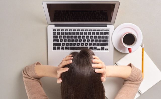 PCを見て頭を抱える女性